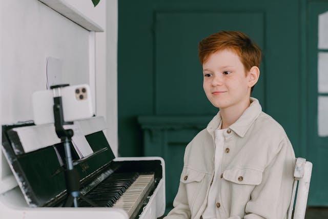 european boy sitting at a piano looking at a camera recording